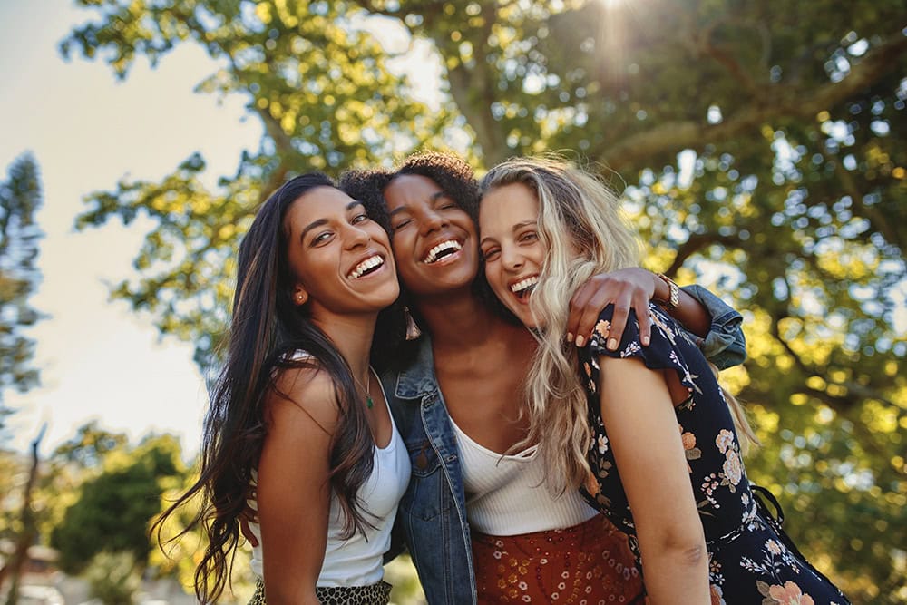 A group of three friends are smiling and hugging each other