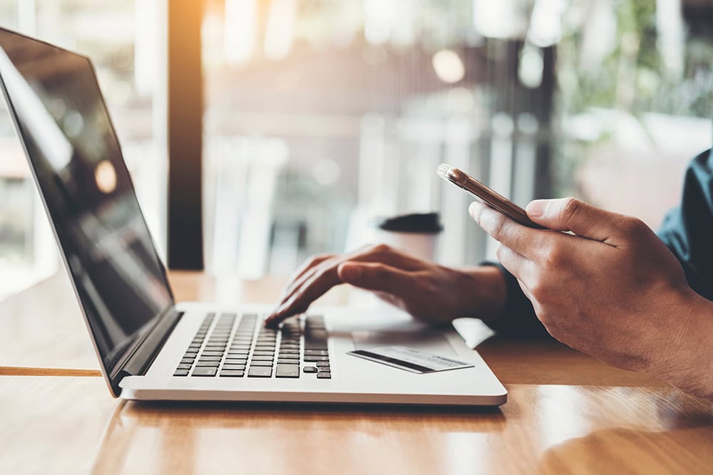 A person is out of the frame but their hands are typing on their laptop and holding their credit card