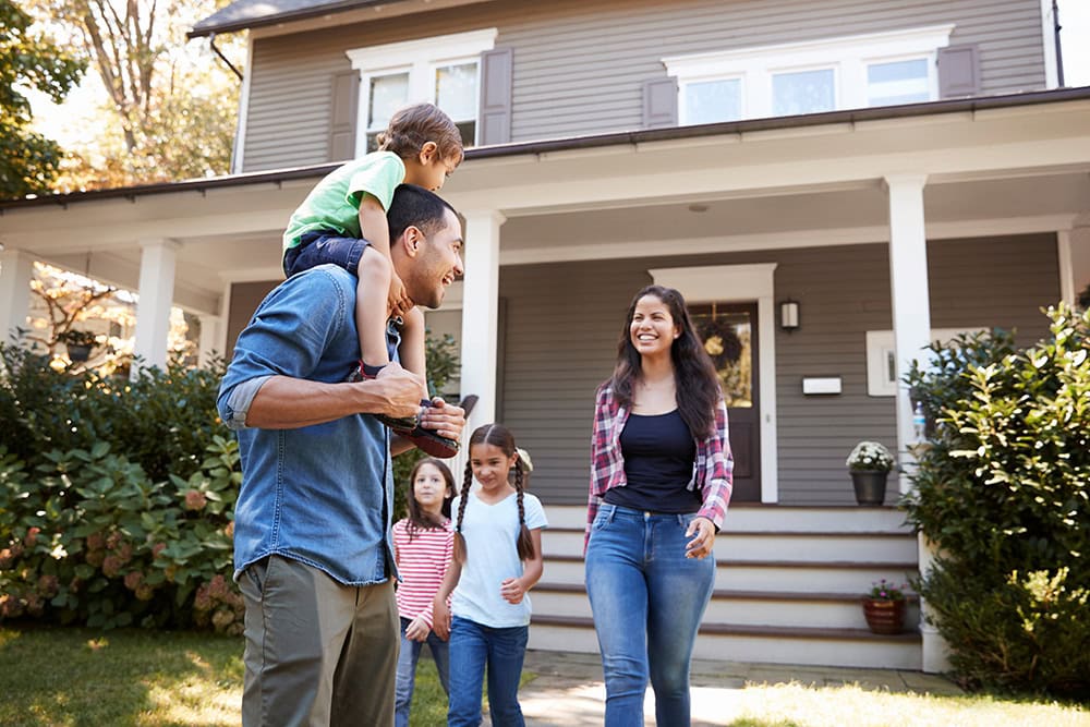 A family descends the front steps of their home. They are smiling at each other.