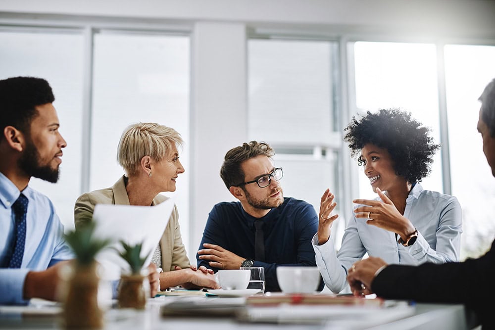 A group of colleagues sit together at a table and are speaking to one another