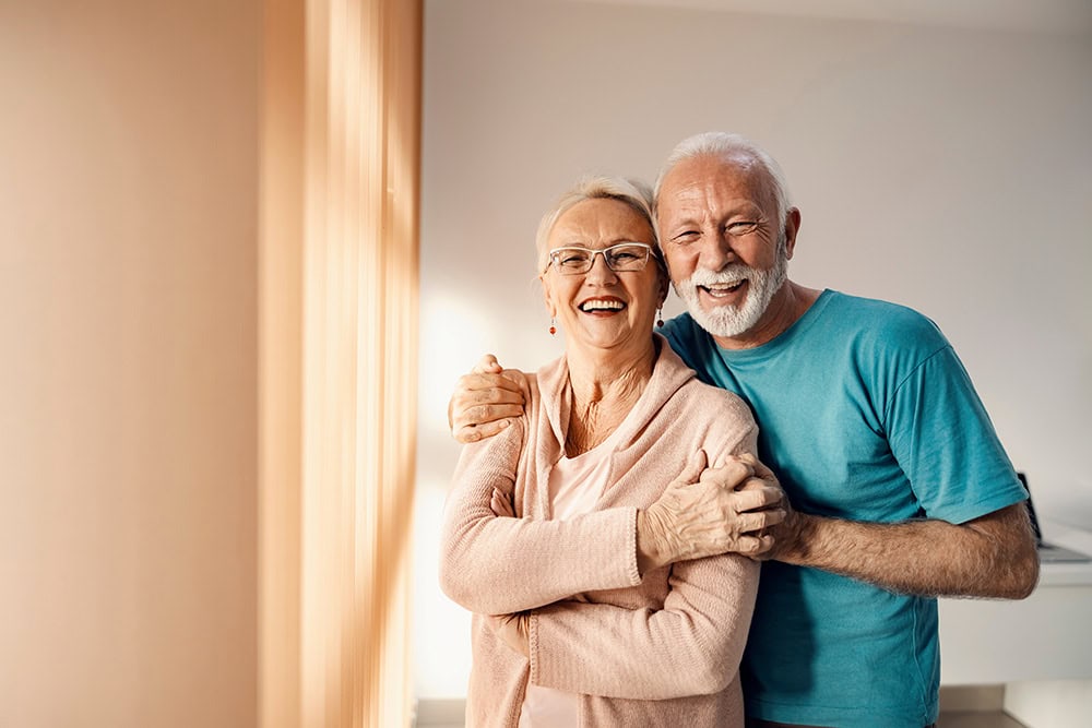 An older couple stand smiling and embracing each other