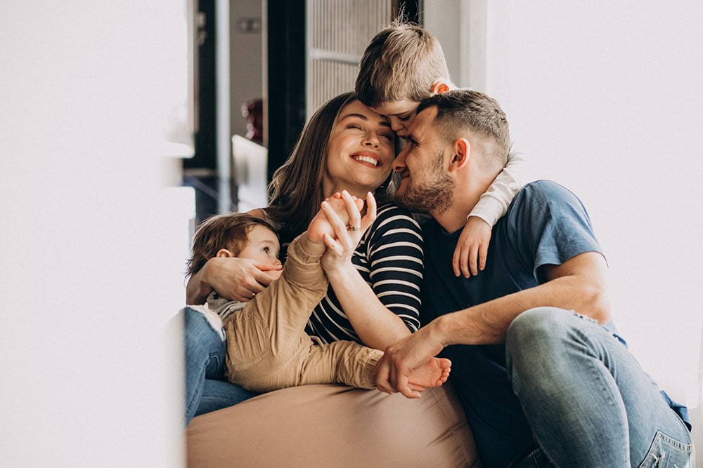 A family of four is sitting together smiling and embracing each other