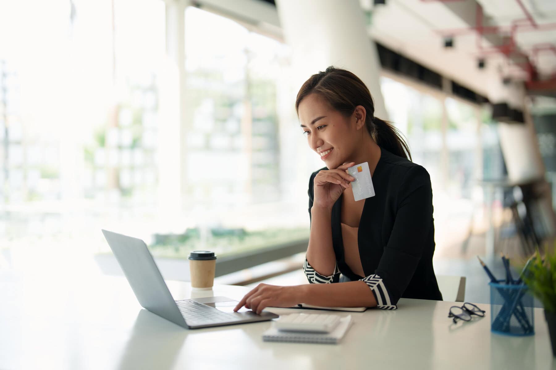 A woman sitting at a table on her laptop and holding her credit card