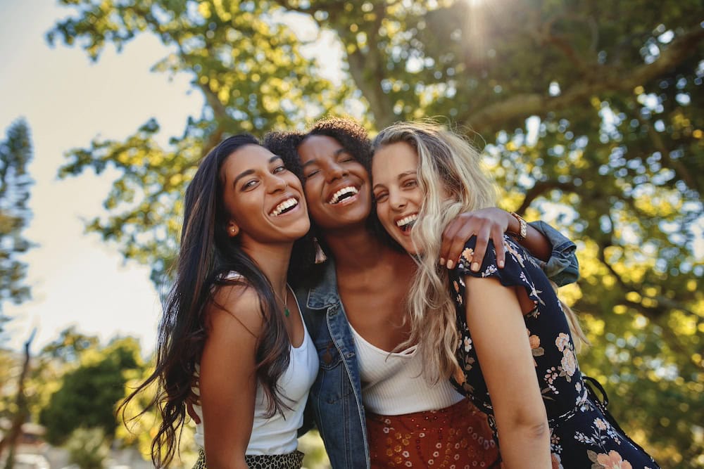 three friends laughing and hugging outside