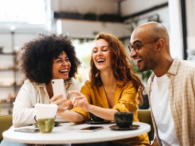 A group of friends is smiling and laughing together while looking at a phone