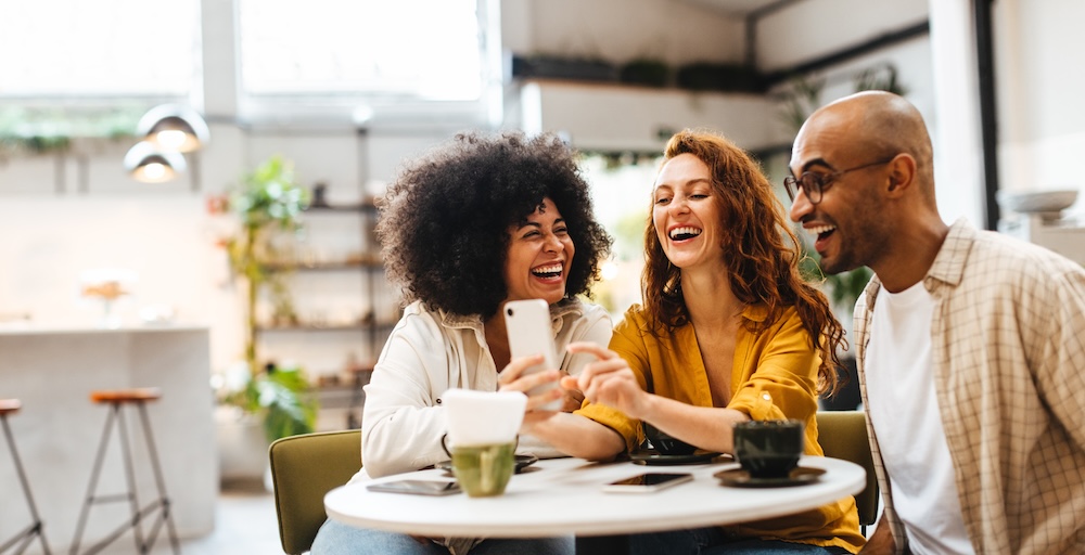 A group of friends is smiling and laughing together while looking at a phone