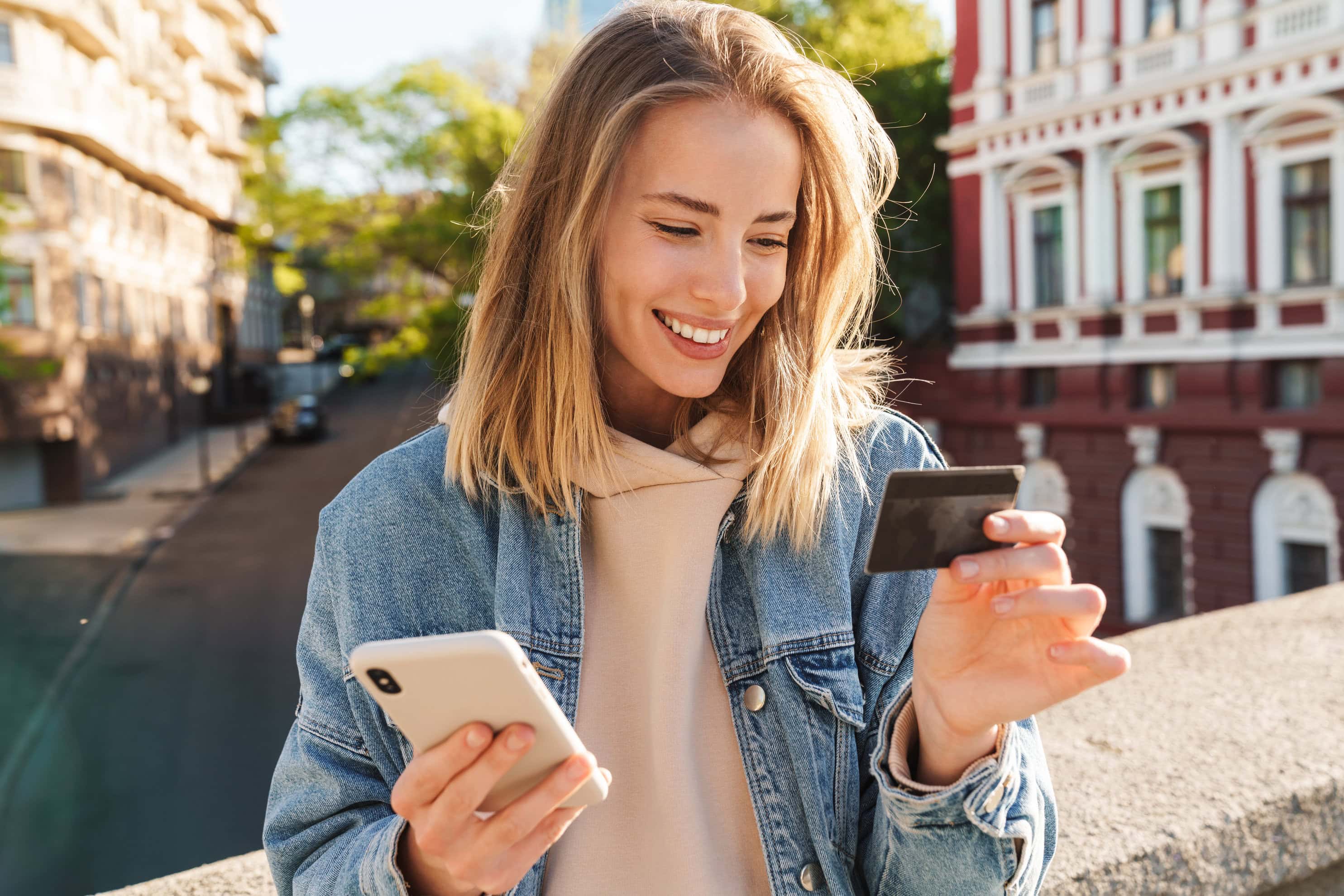 Cheerful young blonde girl shopping online with mobile phone